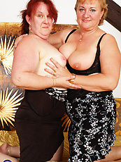 Mature naked duo kneeling in spread pose with saggy tits, bushy pussy and visible dildo
